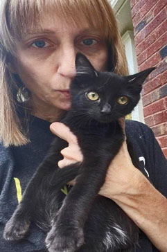 A black kitten is snuggled by a Pippi's Place volunteer.  